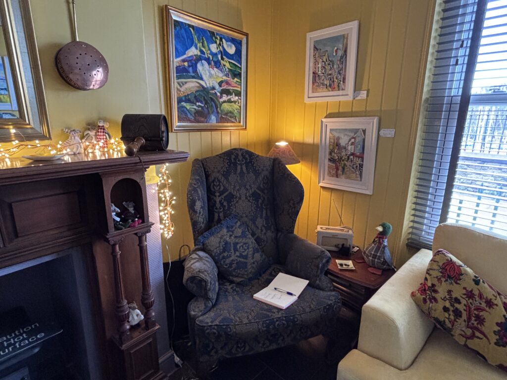Large wing chair in the corner by the fireplace surrounded by original art